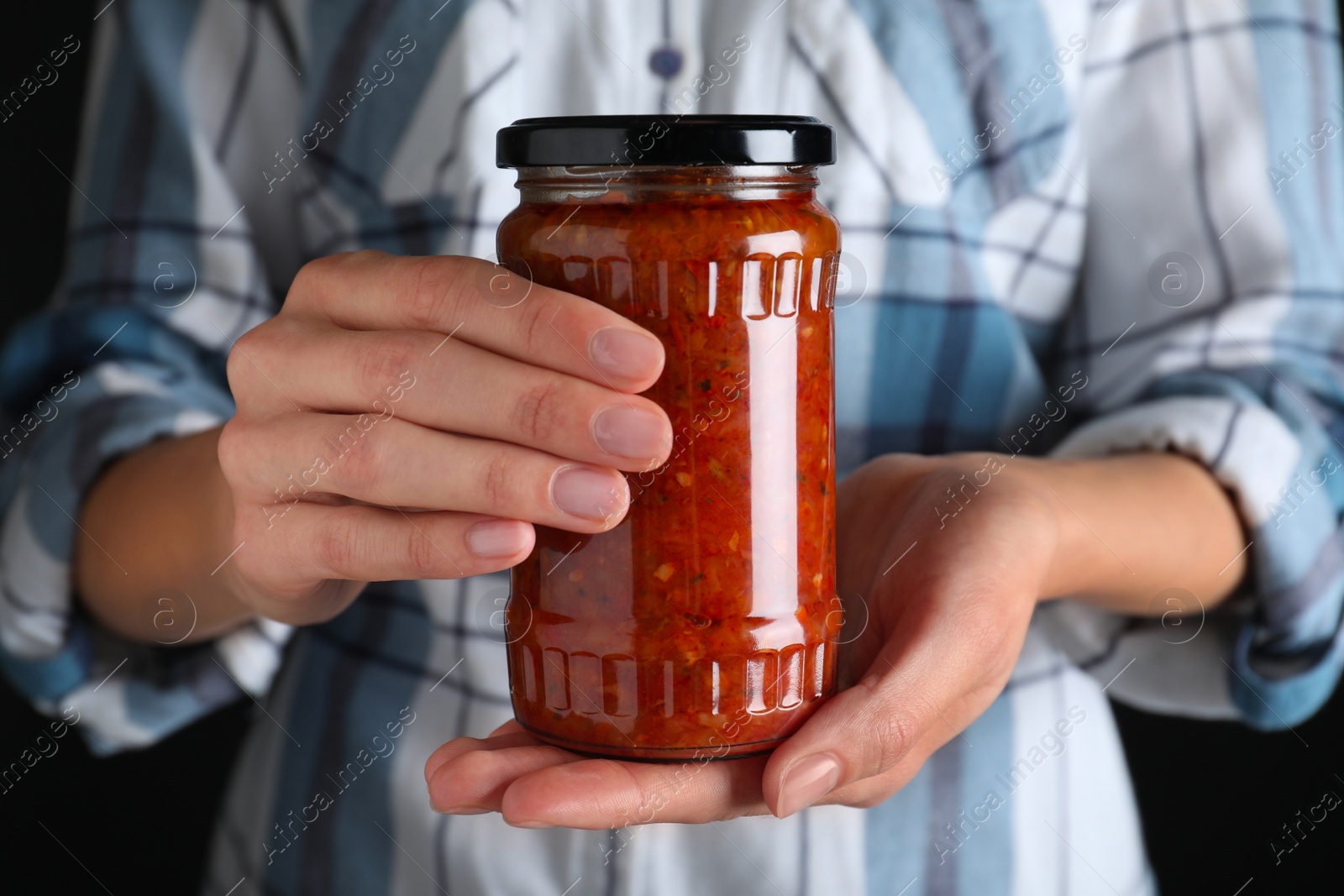 Photo of Woman holding jar with pickled red sauce against black background, closeup