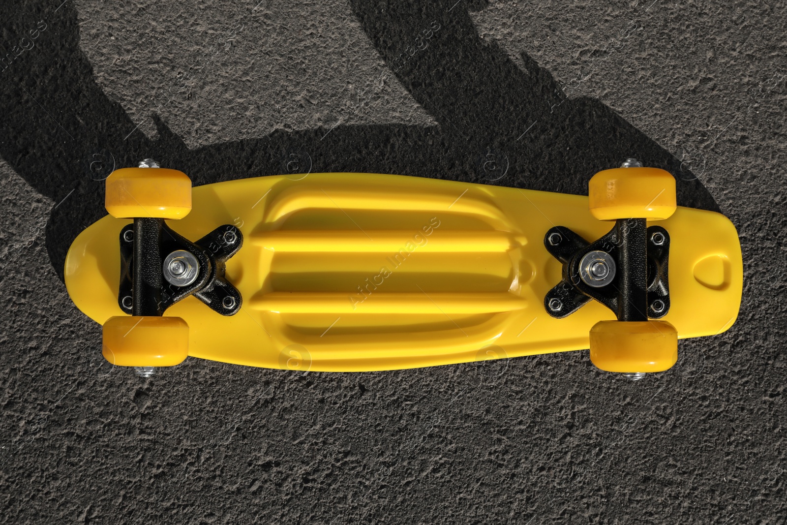 Photo of Modern yellow skateboard on asphalt road outdoors, top view