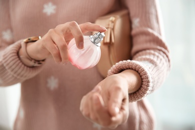 Young woman using perfume indoors, closeup