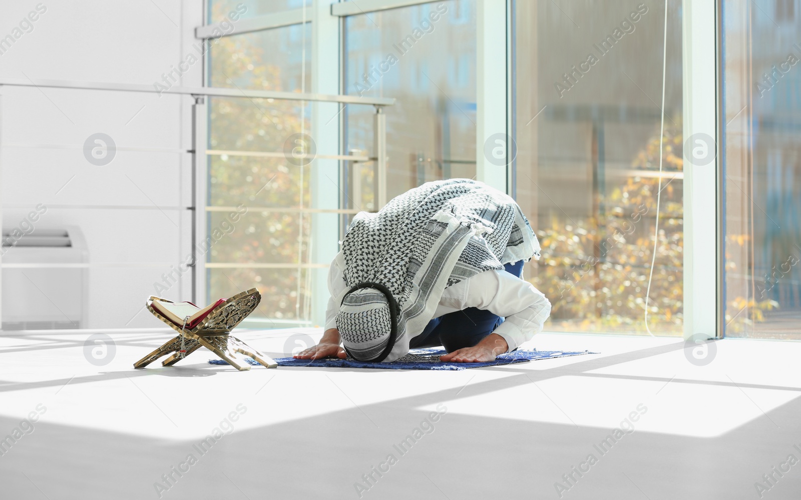 Photo of Muslim man with Koran praying on rug indoors