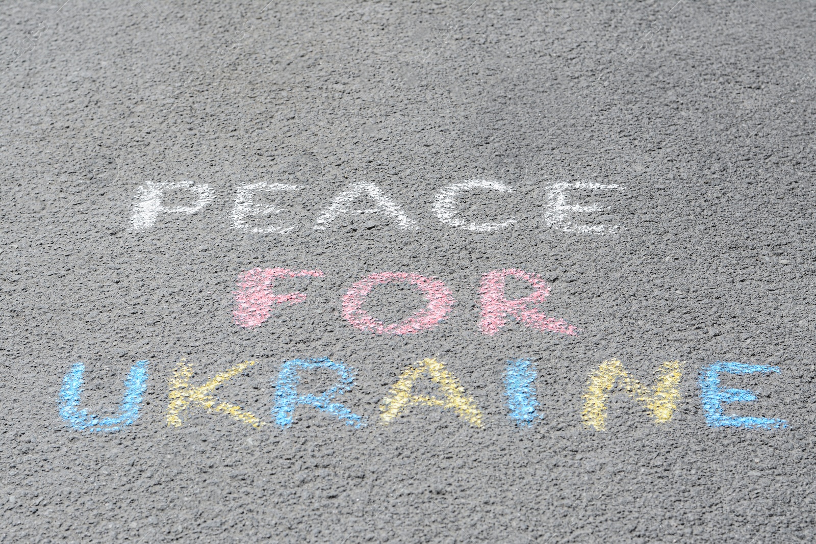 Photo of Words Peace For Ukraine written with colorful chalks on asphalt outdoors