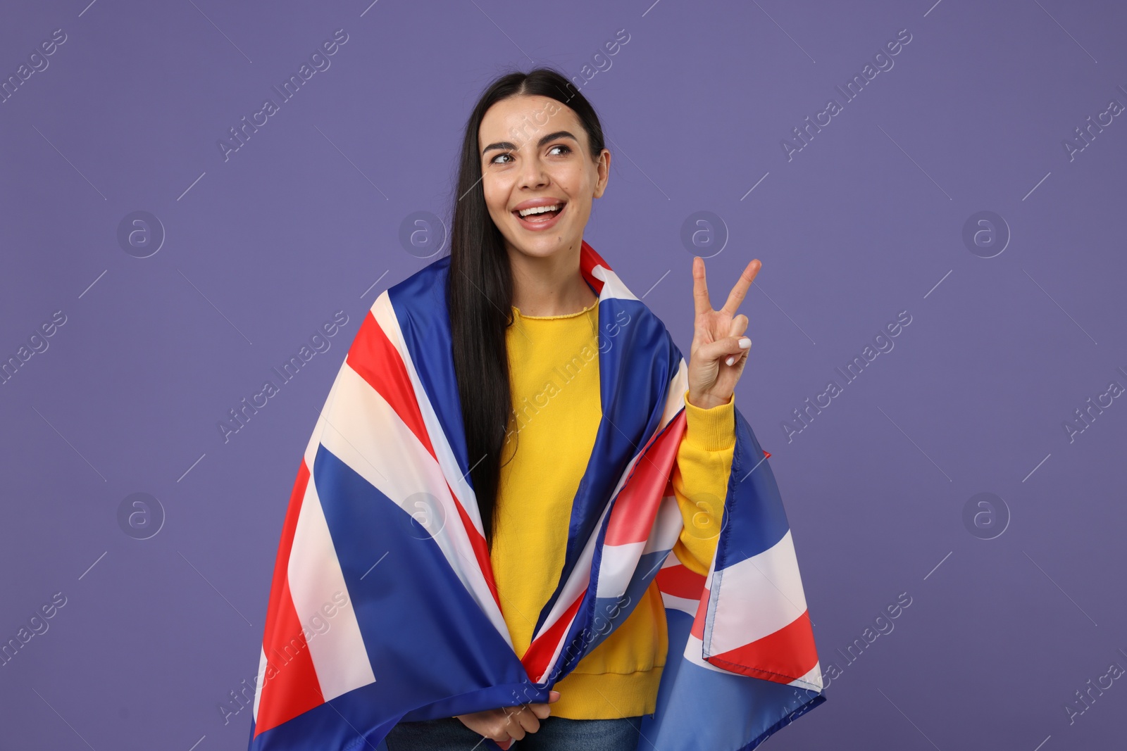 Photo of Happy young woman with flag of United Kingdom showing V-sign on violet background