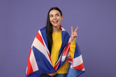 Happy young woman with flag of United Kingdom showing V-sign on violet background