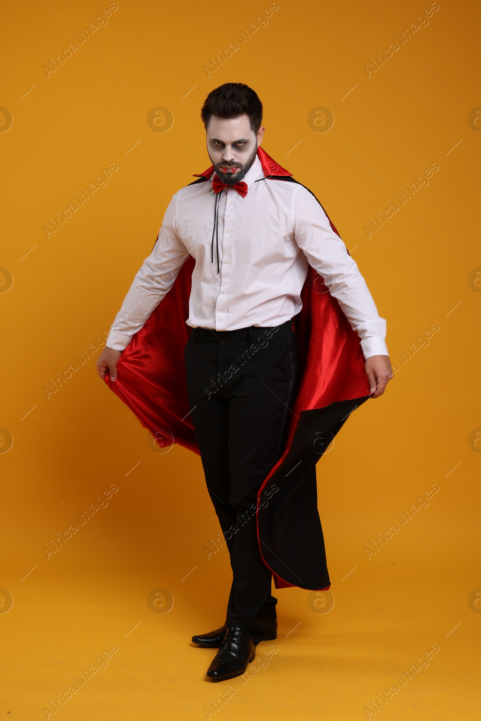 Photo of Man in scary vampire costume with fangs on orange background. Halloween celebration