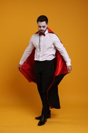 Man in scary vampire costume with fangs on orange background. Halloween celebration