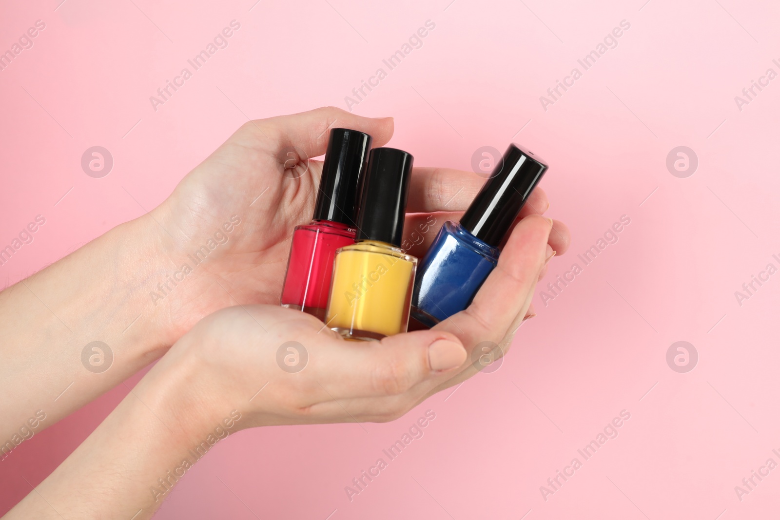 Photo of Woman holding nail polishes on pink background, closeup