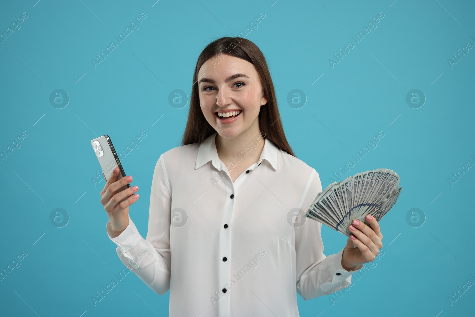 Photo of Happy woman with dollar banknotes and smartphone on light blue background