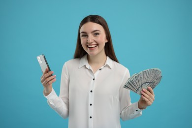 Happy woman with dollar banknotes and smartphone on light blue background