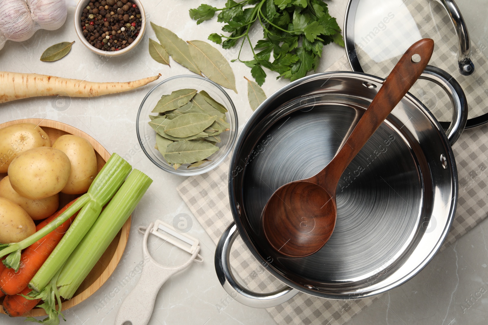 Photo of Pot with ladle and different ingredients for cooking tasty bouillon on light table, flat lay
