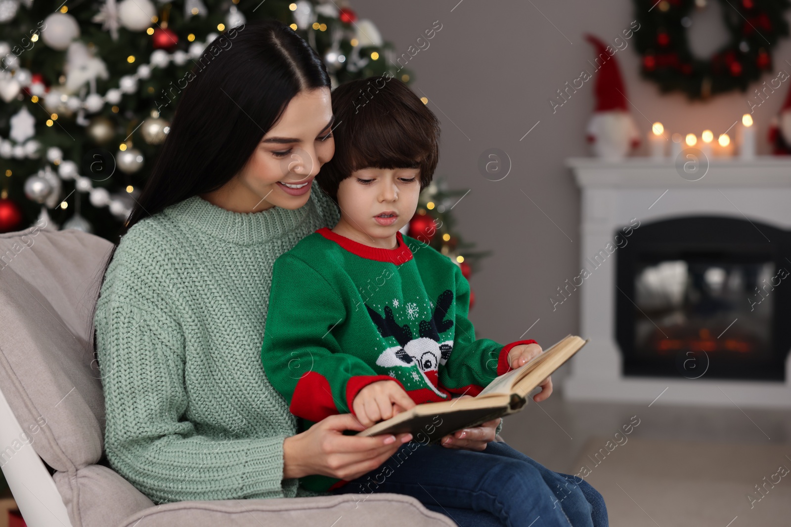 Photo of Mother with her cute son reading book in room decorated for Christmas