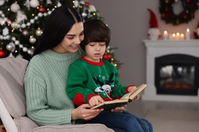 Photo of Mother with her cute son reading book in room decorated for Christmas