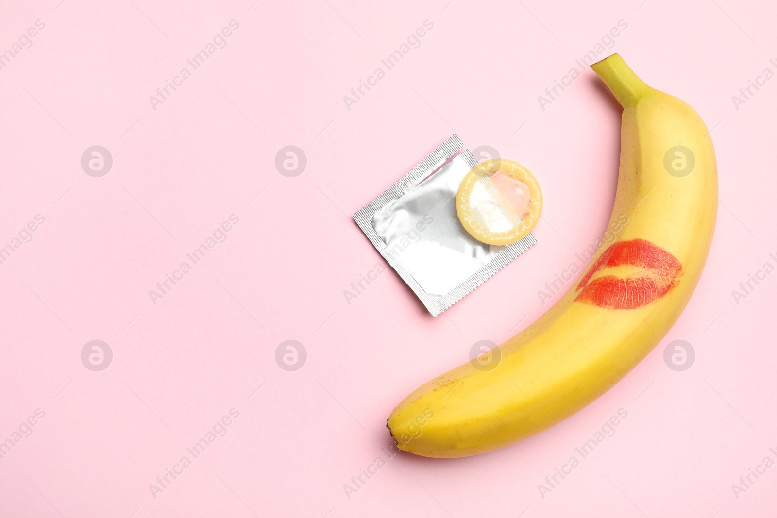 Photo of Condom, banana with lipstick kiss mark and space for text on pink background, flat lay. Safe sex