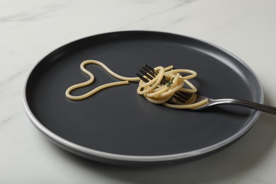 Photo of Heart made of tasty spaghetti and fork on white marble table