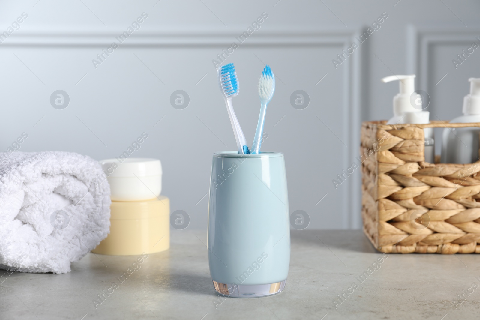 Photo of Plastic toothbrushes in holder, towel and cosmetic products on light grey table