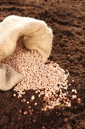 Granulated fertilizer in sack on soil, closeup