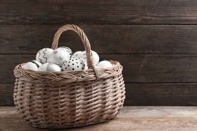 Photo of Basket of Easter eggs on table against wooden background. Space for text
