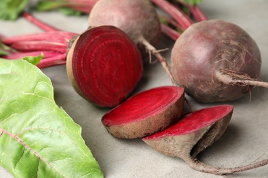 Photo of Cut and whole raw beets on light grey table, closeup
