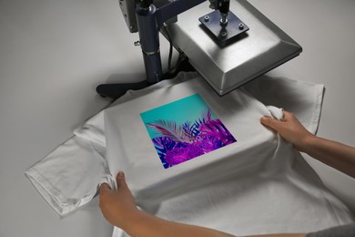 Image of Custom t-shirt. Woman using heat press to print image of bright tropical leaves
