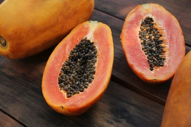 Photo of Fresh ripe cut and whole papaya fruits on wooden table, closeup