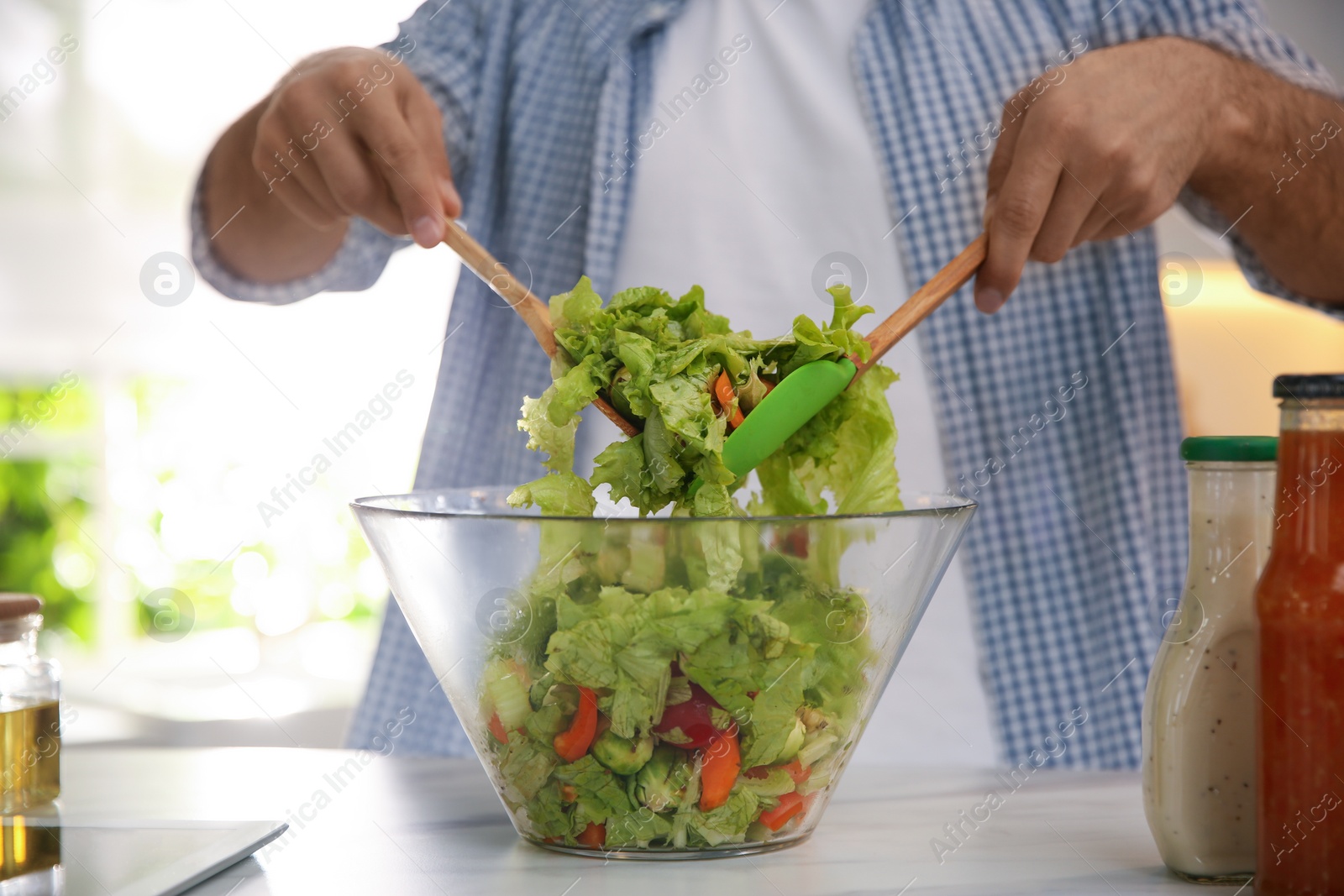 Photo of Man with tablet cooking salad at table in kitchen, closeup