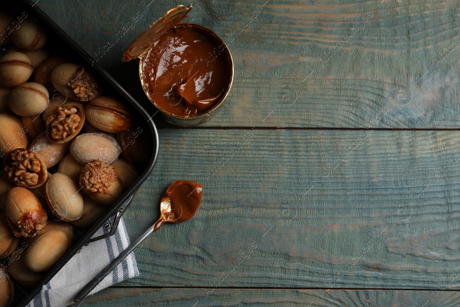 Photo of Freshly baked homemade walnut shaped cookies and boiled condensed milk on wooden table, flat lay. Space for text