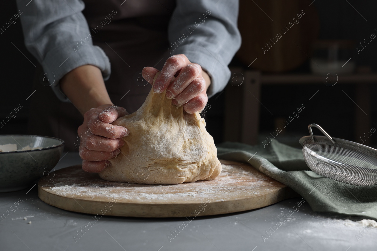 Photo of Woman kneading dough at grey table, closeup