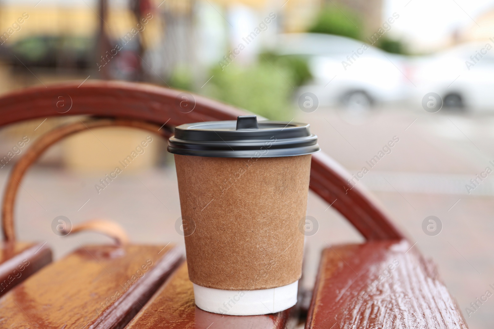 Photo of Paper cup of coffee on wooden bench outdoors. Takeaway drink