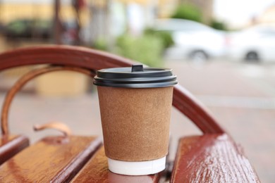 Paper cup of coffee on wooden bench outdoors. Takeaway drink