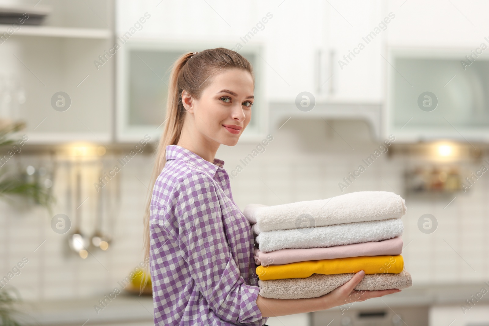 Photo of Woman holding folded clean towels in kitchen. Laundry day