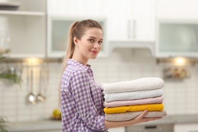 Woman holding folded clean towels in kitchen. Laundry day