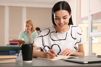 Photo of Young woman studying at table in library