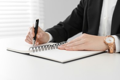 Photo of Woman writing in notebook at white table, closeup