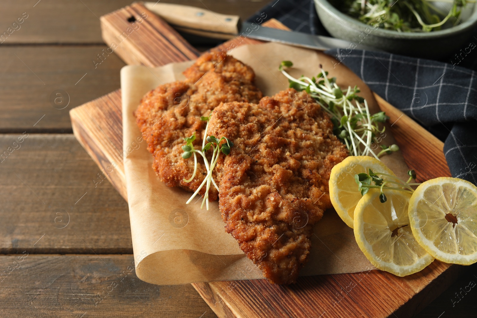 Photo of Tasty schnitzels served with lemon and microgreens on wooden table, closeup
