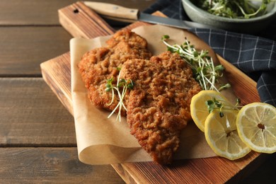 Tasty schnitzels served with lemon and microgreens on wooden table, closeup