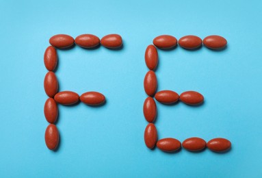 Chemical element Fe made of pills on turquoise background, flat lay. Anemia treatment