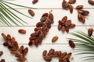 Photo of Sweet dried dates with palm leaves on white wooden table, flat lay