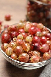 Photo of Bowl of fresh ripe gooseberries on wooden table, closeup