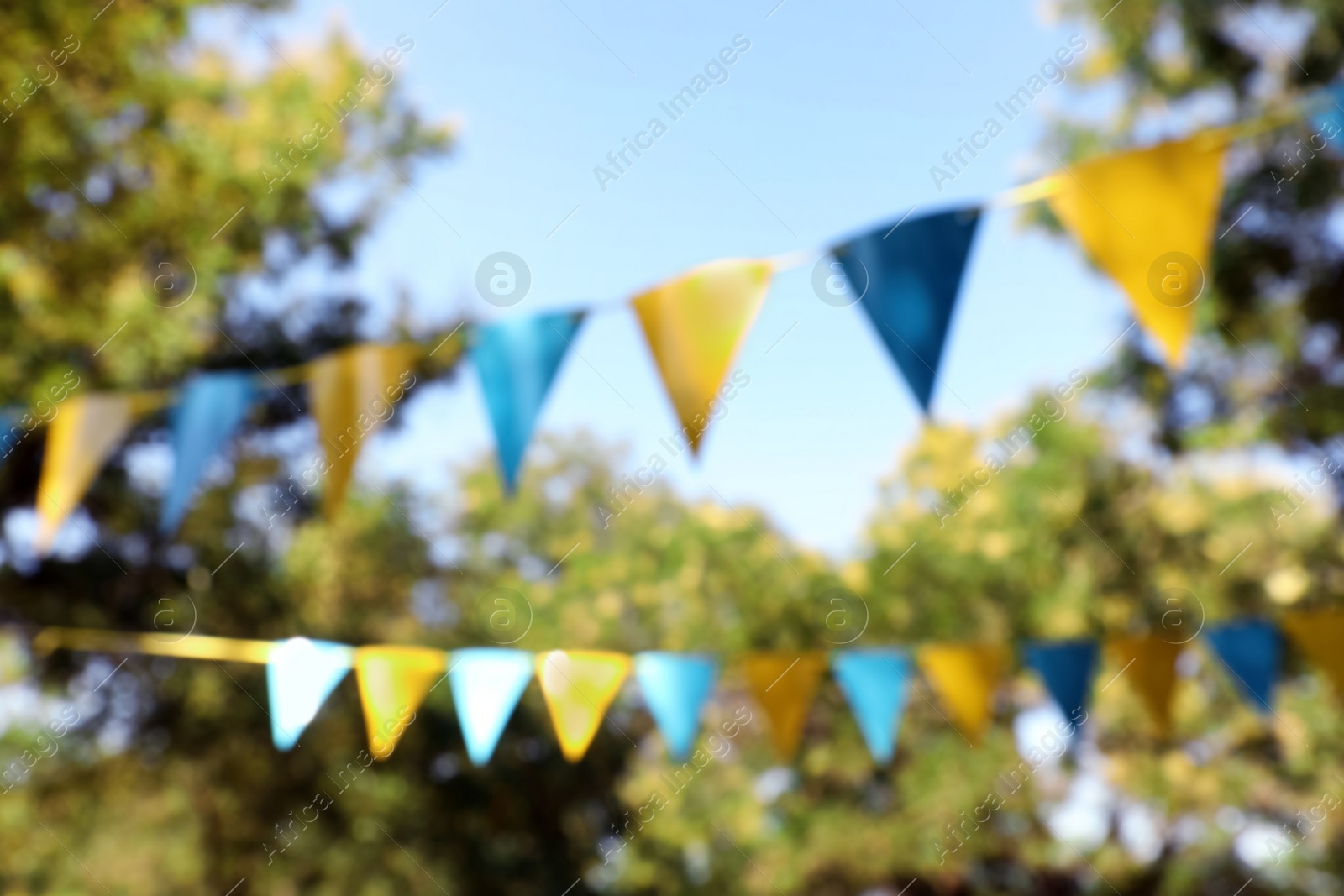 Photo of Blurred view of colorful bunting flags in park. Party decor