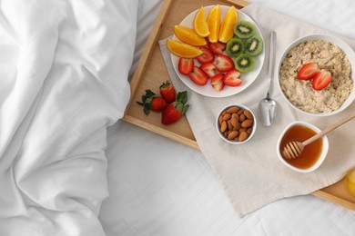 Photo of Tasty breakfast served in bed. Oatmeal, fruits, almonds and honey on tray, top view