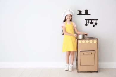 Photo of Little child in chef hat playing with carton stove indoors