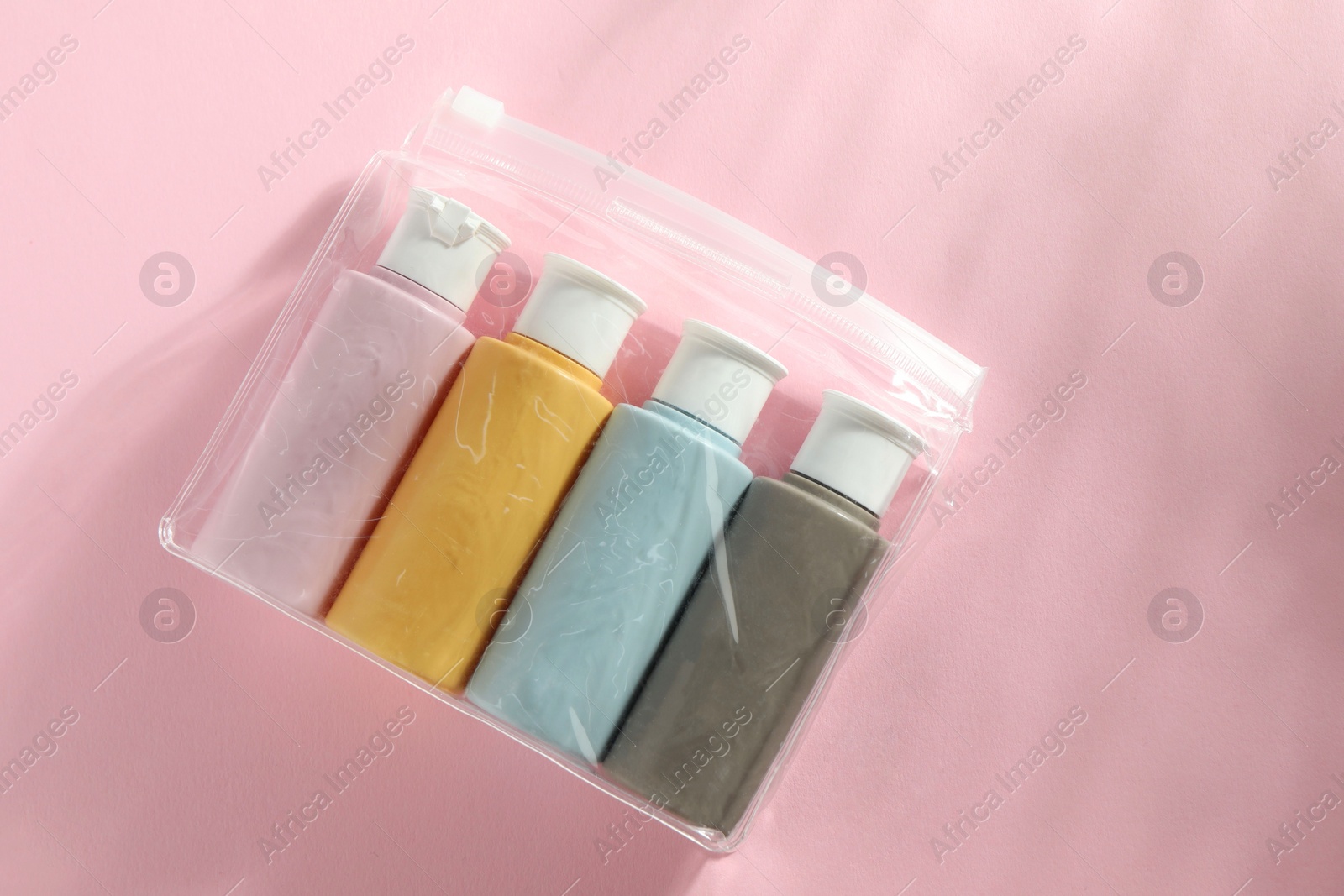 Photo of Cosmetic travel kit in plastic bag on pink background, top view. Space for text