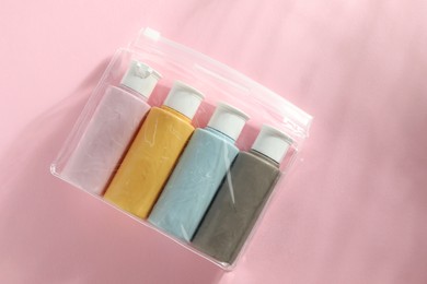 Photo of Cosmetic travel kit in plastic bag on pink background, top view. Space for text