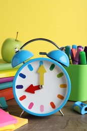 Photo of Light blue alarm clock and different stationery on wooden table against yellow background. School time