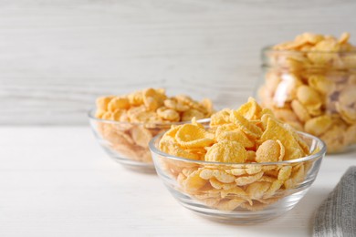 Glass bowl of tasty crispy corn flakes on white wooden table, space for text
