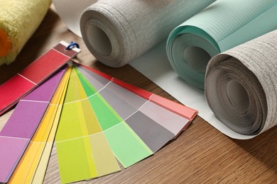 Photo of Different wallpaper rolls and color palette samples on wooden table, closeup