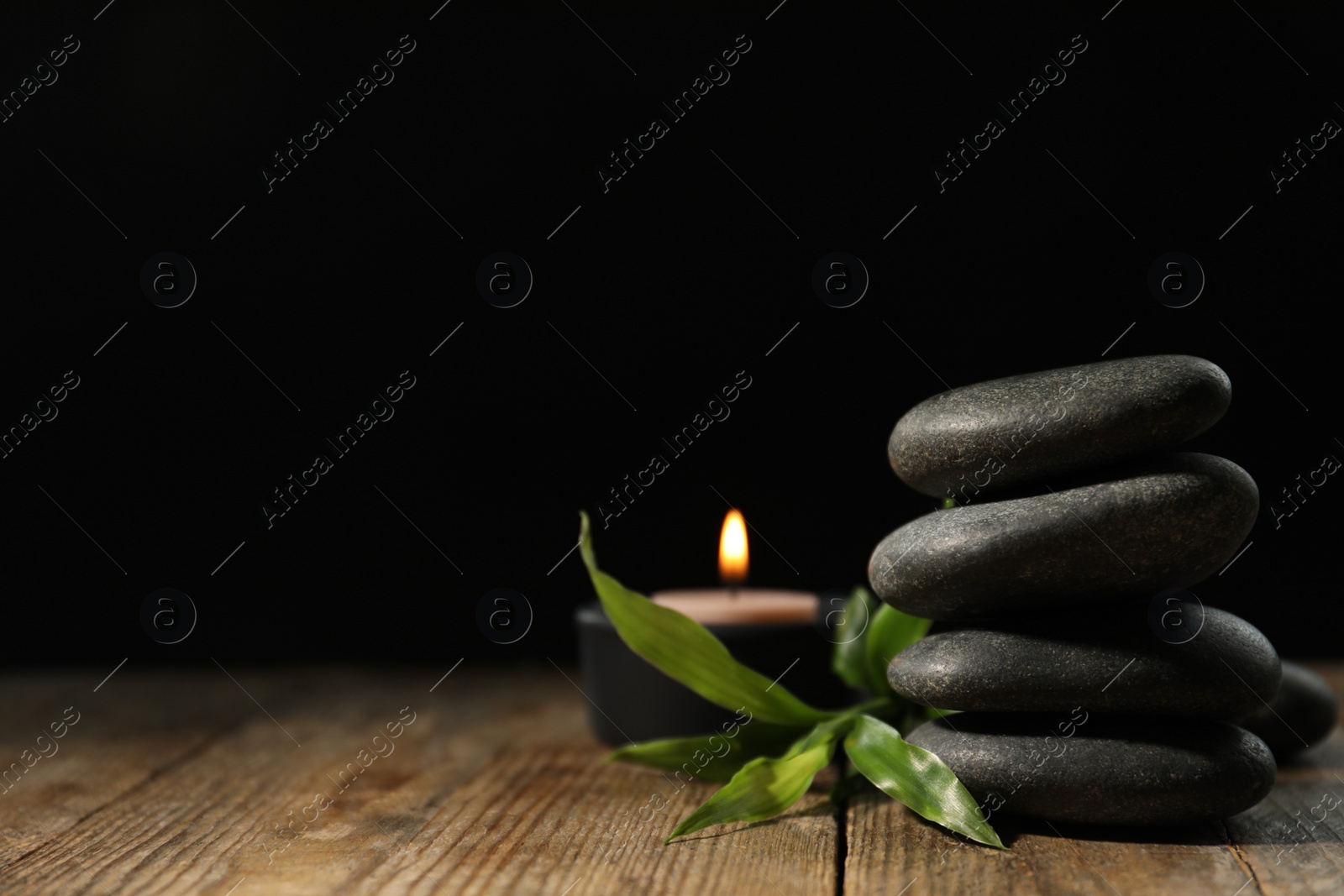Photo of Spa stones, bamboo sprout and candle on wooden table against dark background, space for text
