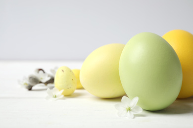 Colorful Easter eggs and flowers on white wooden table, closeup