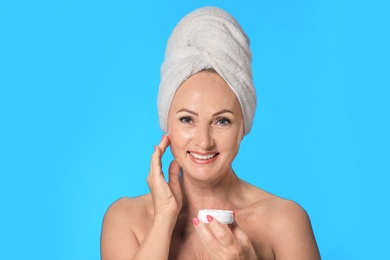 Portrait of beautiful mature woman with perfect skin holding jar of cream on light blue background