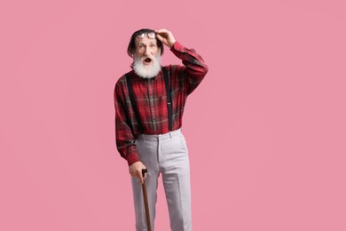 Surprised senior man with walking cane on pink background