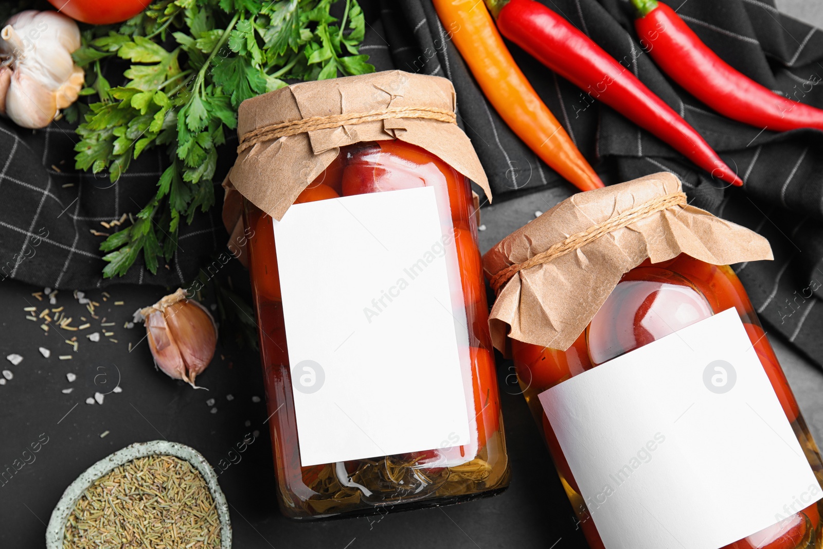 Photo of Jars of pickled tomatoes with blank stickers on black table, flat lay